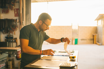 Focused craftsman counting expenses in joinery workshop