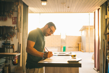 Focused craftsman counting expenses in joinery workshop