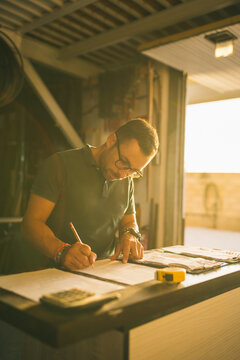 Focused craftsman counting expenses in joinery workshop