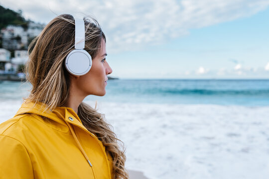 Woman in wireless headphones contemplating nature of beach
