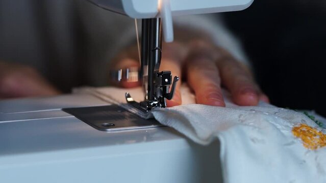 Slow motion of hands sewing white fabric with a machine