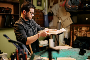 Portrait of leather craftsman makes a leather motorcycle seat at table in workshop studio