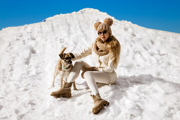 Beautiful stylish woman playing with her dog in the snow in winter scenery in the mountains. Winter...