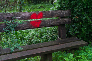 Bright red heart painted on the back of a wooden bench in the park