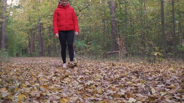 Caucasian female walking on a dirt trail while kicking the fallen dry leaves in the woods