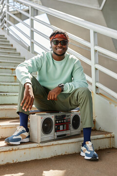 Vertical portrait of young black man wearing street style clothes posing outdoors with boombox