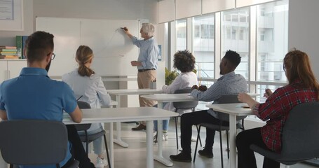 Senior teacher explaining diagram written on whiteboard while diverse college students sitting at desk - Powered by Adobe