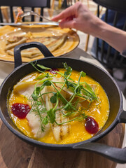 Creamy autumn dish pumpkin soup with sauteed squid and pea sprouts in black saucepan, close-up.