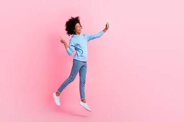 Fototapeta na wymiar Full size portrait of carefree little girl jumping hold telephone make selfie show v-sign isolated on pink color background