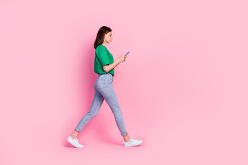 Fototapeta na wymiar Full length photo of nice young girl walking hold device chatting read news dressed trendy green clothes isolated on pink color background