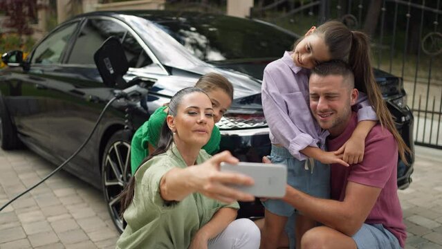 Family taking selfie in front of electric car in driveway.