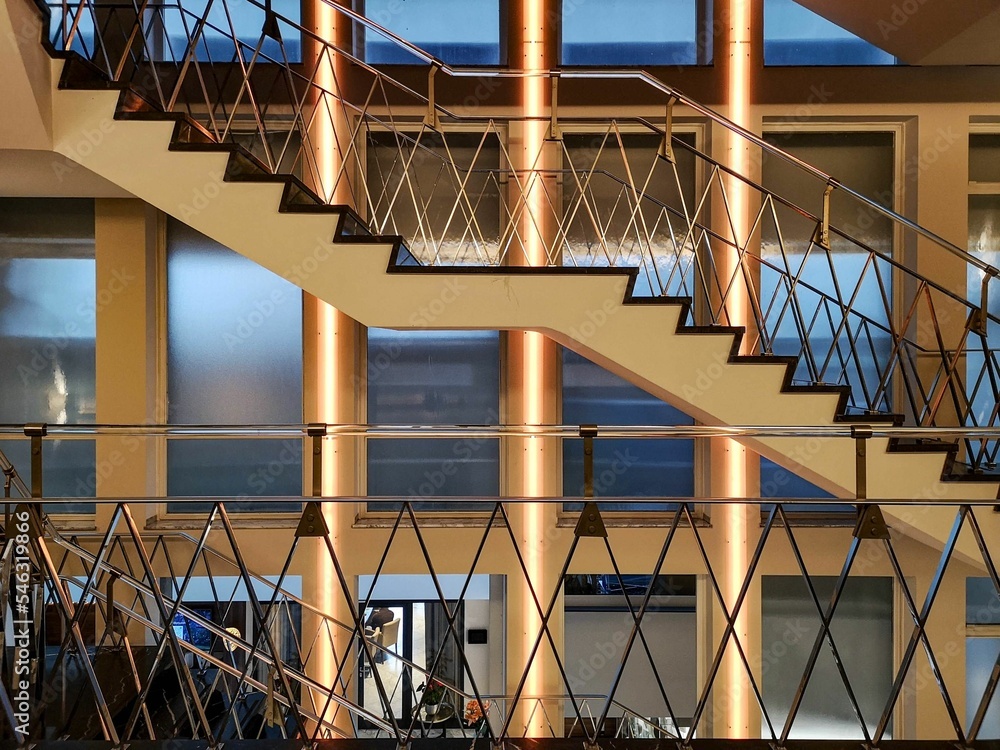 Poster view of architectural modern building with stairs with metal railings in front of golden columns