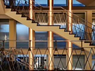 View of architectural modern building with stairs with metal railings in front of golden columns