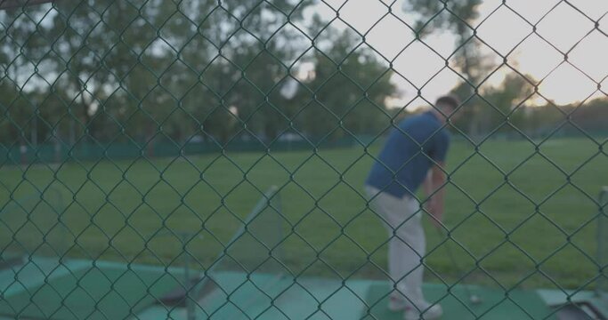 Closeup shot of a golf player through a metallic net at Adi Ciganlija, purple sky, trees background