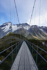 Vertical high-angle of a wooden suspended bridge leading to the ridged, snowy mountains