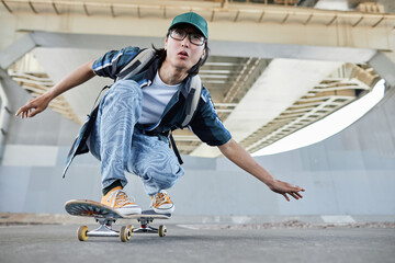 Dynamic full length shot of young Asian man skateboarding outdoors in urban setting moving to camera