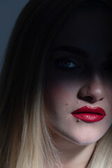 Fashion and make-up concept. Beautiful blonde woman portrait partly face covered with shadow. Mouth and nose illuminated with light. Model looking at camera. Red lipstick make-up