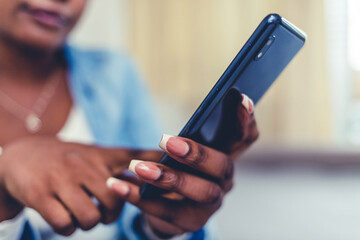 A happy african-american woman sitting on her couch while texting on her phone. Shot of a young professional woman sending a text message on her cellphone.