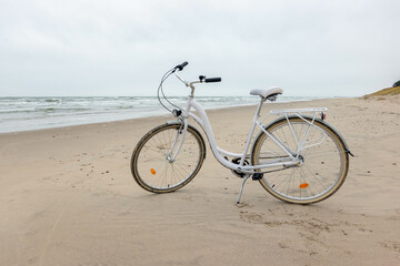Fototapeta na wymiar White bike on the sand by the Baltic sea. Bicycle on the sandy shore, nobody.