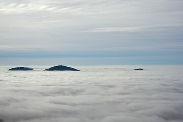 Einzelne Bergkuppen ragen über einem Meer von Wolken heraus und man kann bis zum Horizont sehen