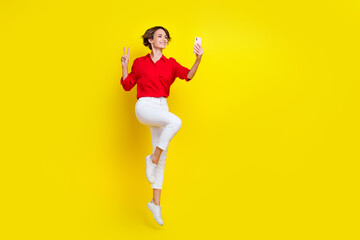 Fototapeta na wymiar Full size portrait of energetic attractive girl jump demonstrate v-sign make selfie isolated on yellow color background