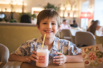 A child drinking a milkshake in a cafe and smiling happily