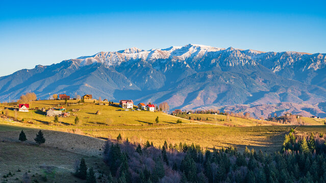 Malerisches Bergdorf Pestera bei Zarnesti in den rumänischen Karpaten mit schneebedeckten Gipfeln im Bucegi Gebirge im Hintergrund