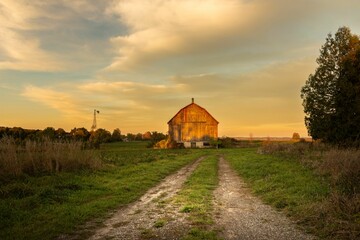 View of tire tracks leading to a barn beneath a warm autumn sky just before sunset