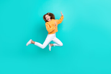Full length photo of sweet charming schoolgirl wear orange sweatshirt jumping high empty space isolated turquoise color background