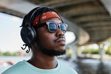 Closeup side view of young black man wearing headphones in urban city setting outdoors