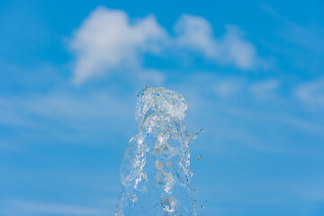 Abstract splash of water up in the air against blue sky with clouds