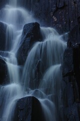 Vertical shot of a waterfall over black rocks