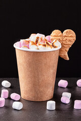 Paper cup with hot drink with marshmallows on dark background. Recycling and eco friendly concept.