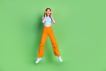 Full length photo of overjoyed pretty person jumping hands touch headphones isolated on green color background