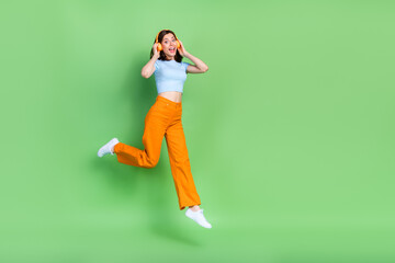 Fototapeta na wymiar Full size portrait of cheerful excited girl jump arms touch headphones empty space isolated on green color background
