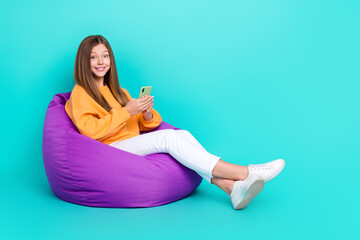 Full length photo of pretty shiny schoolgirl wear orange sweatshirt bean bag chatting device empty...