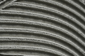 Cementitious adhesive applied to floor or wall ready to receive the ceramic tile. Ceramic tile adhesive, mortar with patterns of notched trowel. Macro shot of cement putty texture with stripes.