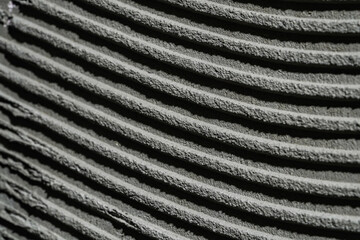 Pattern of notched trowel strokes on the gray surface of cement putty for laying ceramic tiles. Texture of glue paste with strokes and stripes. Macro shot of a wall surface with cement.