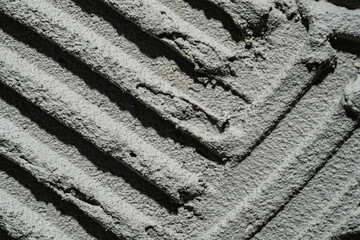 Pattern of notched trowel strokes on the gray surface of cement putty for laying ceramic tiles....