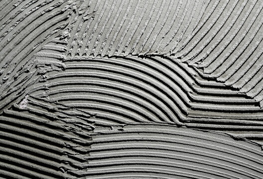 Gray wall glue plaster comb surface prepared for tiling. Tile adhesive notched trowel patterns. Texture background of tile mortar paste. Grey cement wall with a linear pattern. Macro shot.