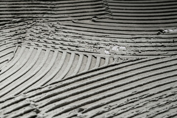 Gray wall glue plaster comb surface prepared for tiling. Tile adhesive notched trowel patterns. Texture background of tile mortar paste. Grey cement wall with a linear pattern. Macro shot.