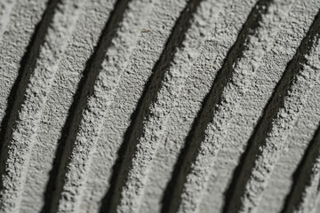 Fresh concrete tehture with patterns of notched trowel. Macro shot of grey surface cement putty on wall with lines or strokes stripes. Uneven adhesive mortar paste for ceramic tiles. Tile installation
