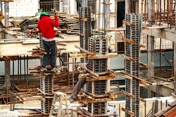 A construction worker nails wood poles as temporary supports to steel formwork for concrete columns.