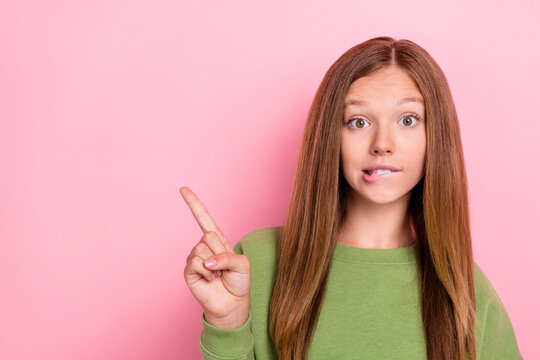 Photo of curious nice girl with straight hairstyle wear green sweater directing empty space biting lip isolated on pink color background