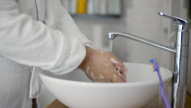 Cropped shot of man in bathrobe washing hands in bathroom at home. Realtime