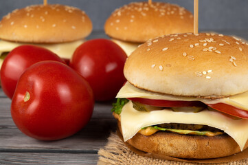 A toasted sesame bun hamburger with pickles and ripe tomatoes. White leaves of melted cheese stick out.