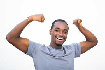 Cheerful young black man flexing his biceps and smiling on white wall