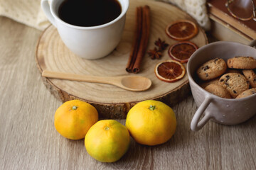 Cup of tea or coffee, various spices, bowl of cookies, tangerines, books, reading glasses and knitted blanket on wooden table. Hygge at home concept, selective focus.