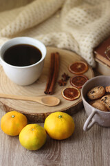 Cup of tea or coffee, various spices, bowl of cookies, tangerines, books, reading glasses and knitted blanket on wooden table. Hygge at home concept, selective focus.