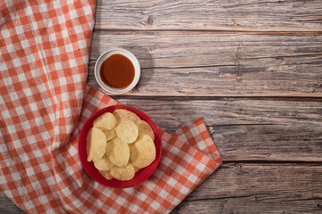 Potato chips and hot sauce on wooden table with tablecloth